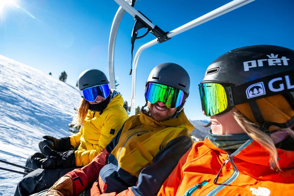 Trois skieurs souriants sur un télésiège, au soleil